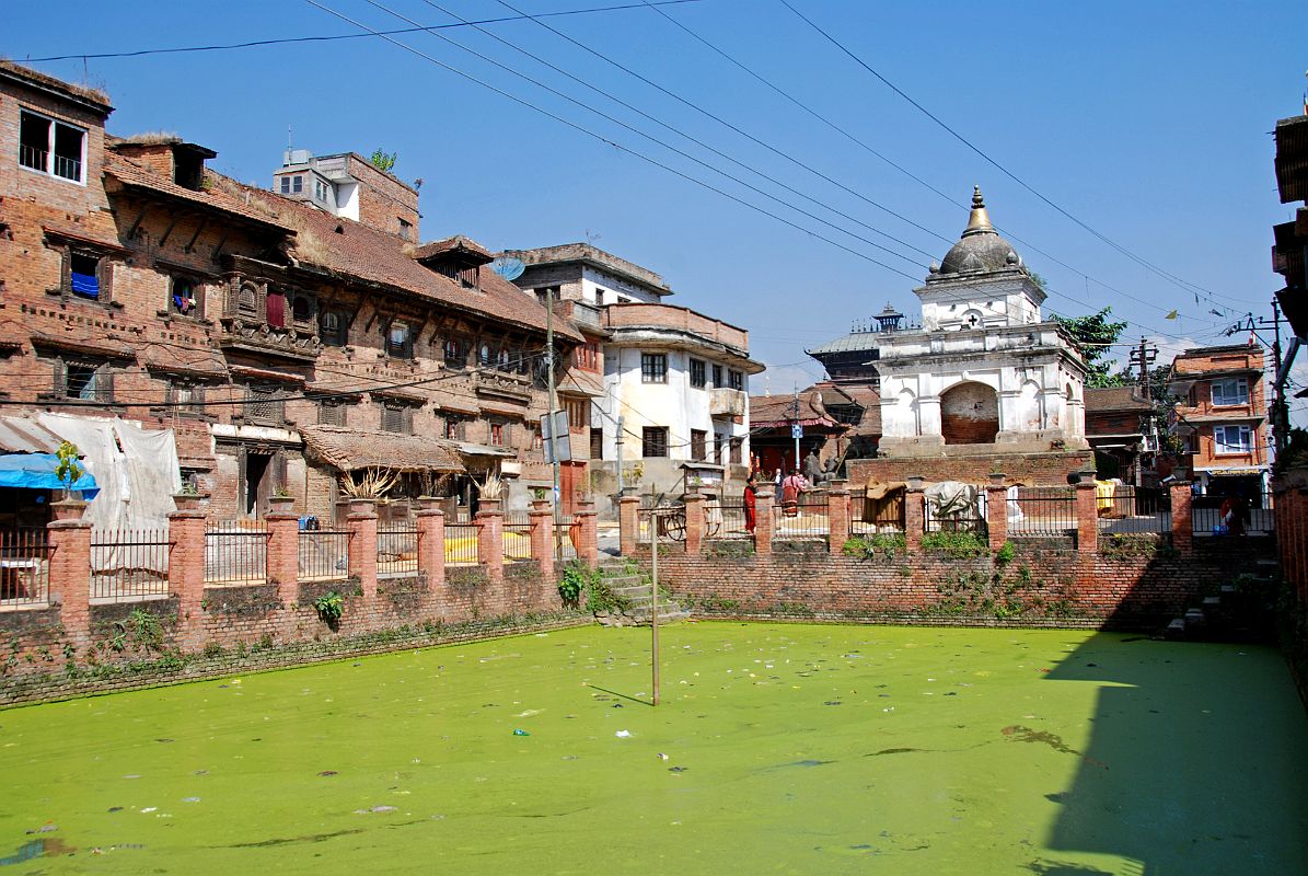 Kathmandu Valley 2 Kirtipur 03 Pond In Village Square, Former Royal Palace, Small Temple A walking tour through the winding streets of Kirtipur near Kathmandu offers a stroll into the past. Cobble stones, charming brick houses, carved wood windows, and inhabitants in homespun attire. The central Kirtipur square across from the entrance to the Bagh Bhairav Temple was the former royal residence, and has a pond with brackish green water and a small temple.